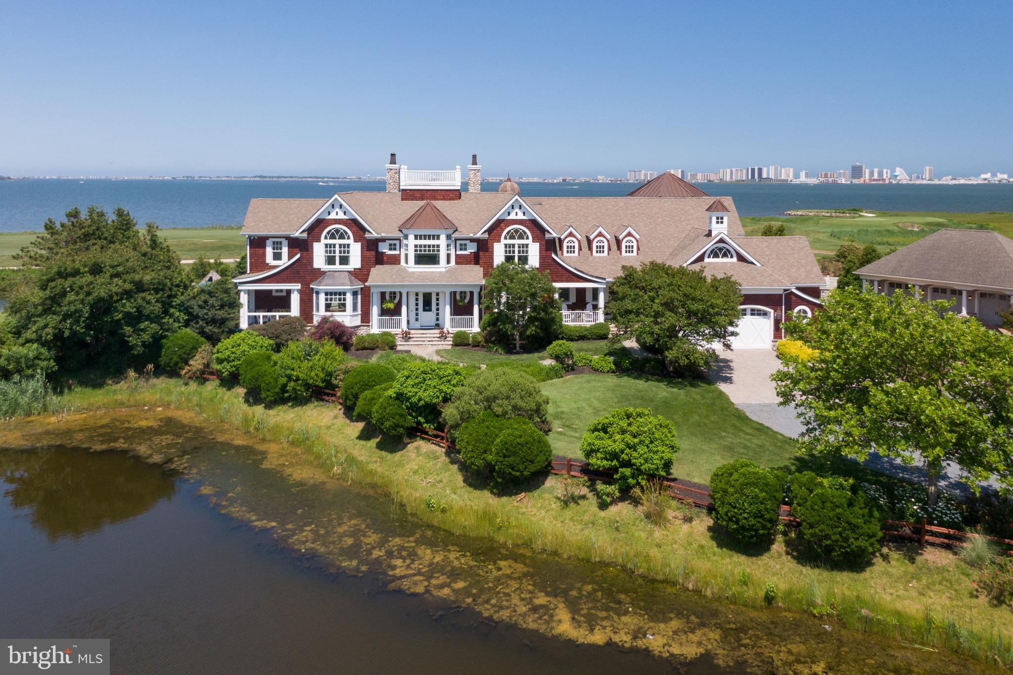 Award winning estate…this crown jewel of the Eastern Shore’s coastal corridor is situated on an acre of land overlooking indigenous habitat ponds, Links of Lighthouse Sound 4th,5th and 6th fairways and the stunning panoramic view of Assawoman Bay and the Ocean City Skyline. A collaboration of NYC and Washington DC design teams along with local artisans, this property is truly a work of art. It begins as you drive onto the stone bridge entrance, one will begin to appreciate the blend of beauty of this Hamptons-style, cedar shingled home and the Eastern Shore way of life. All rooms within the home offer stunning architectural elements and have spectacular views of Coastal natural habitats. Through the main entrance of the home, you step into an elegant foyer and beyond is the spacious living room offering a 20’ceiling, stunning picture window and commissioned aged glass mirror above the limestone fireplace. The billiard room and den features custom Honduran Mahogany woodwork throughout, full bar area with granite countertops and side porch. To the right of the foyer is an elegant dining room featuring Gracie hand-painted wallpaper depicting paintings of our local Audubon setting. The bay window allows for breathtaking sunsets during evening dining. The chef’s kitchen with Carrara Italian marble, Wolfe appliances and custom tile includes a breakfast room and cozy sitting area. As an extension of the kitchen, the Butler’s pantry features granite countertops, a 120-bottle wine refrigerator, copper sink and separate beverage refrigerator. The 3-story octagonal turret overlooks the 40x16 gated pool and hot tub with hardscape. On the second floor, the primary bedroom offers a gas fireplace, reading area, private balcony, striking ensuite with separate 17’x22’ dressing room. The yoga/flex room has 5 magnificent 5’ circular windows which takes full advantage of the peaceful bay and golf course views. The top-level observatory serves as a perfect home office adding the morning sunrise and Ocean City skyline. Other notable features include walnut floors throughout the home, front and back staircases, pocket doors allowing additional privacy, solid 8’ wood doors, designer silk window treatments, 2 laundry rooms, hand-crafted custom woodwork, 9’ vaulted or extended ceilings, surround sound, 2.5 garage with 220V EV charging station, 4 heating A/C systems, 2 80-gallon hot H2O, rooftop widows watch with spectacular 360-degree, panoramic views. The property also provides easy access to the bay through neighborhood beach and protected cove for small boat anchorage and a 30' floating boat slip at Pines Point Marina.