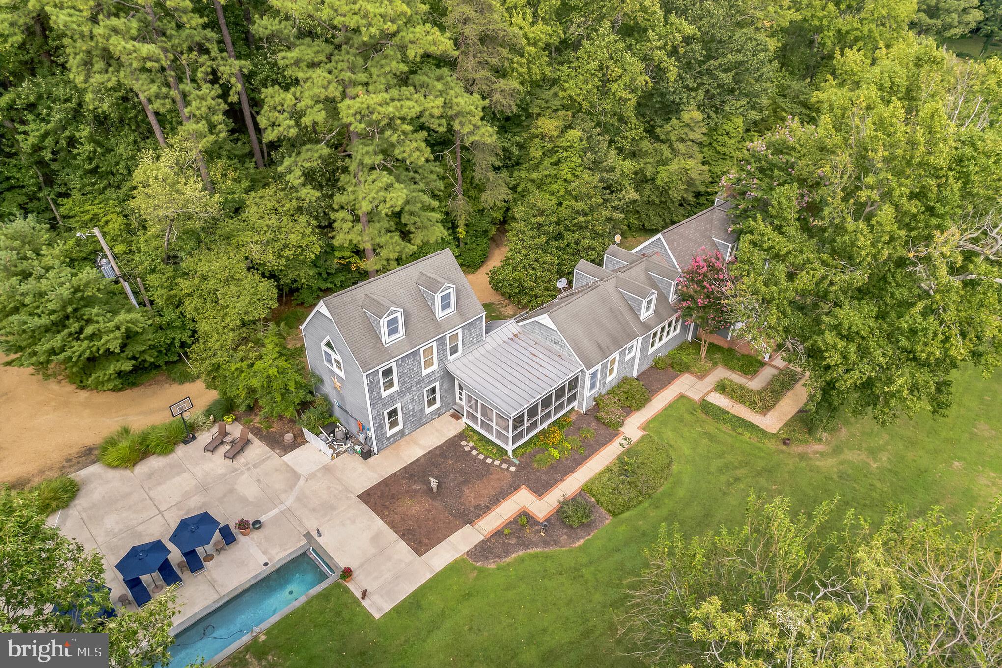 Positioned on Horseshoe Bend of the St. Mary’s River, near St. Mary’s City, you’ll find Cardinal Pines, a beautiful waterfront estate. The location provides views of waters of the bend, which are perfect for boating, kayaking, canoeing, or swimming, while taking in the area’s beauty from sunrise to sunset. This private estate provides a peaceful escape, but also serves as a wonderful impetus for area exploration. Within a quick boat trip are summer getaway hotspots throughout the St. Mary’s River or out the mouth into the Potomac River to the shores of Virginia.  Many points of interest for food, drinks, and live music, or of course the various bodies of water for boating and fishing. Amongst a long list of features making this a unique, truly once-in-a-generation opportunity is the property, residence, and deep-water dock. The wide vista is of the St. Mary’s College of Maryland’s campus, Church Point at Historic St. Mary’s City, and across to Pagan Point and Horseshoe Point.  This 6-acre parcel allows for a seamless launching point to board your power or sailboat in waiting and cruise out for a day or overnight.  The property boasts over 530 ft +/- of shoreline while the home rests approximately 15 ft +/- above the water line. The grounds of this estate consist of mature tree growth, professional landscaping, pier with boat lift and a slip for a sailboat, as well as a swimming pool with tanning ledge and a lap lane.  Cardinal Pines hosts a main residence attached to a two-car garage with a pied-à-terre above and connected by a screened porch.  The Nantucket-style home welcomes you through the front door into a vaulted living room.  The ceiling accentuates the brick, wood-burning fireplace and stunning wood beams. Windows brings water views in as well as light from above.  The dining room is just off the kitchen and allows for great gatherings.  The loft above the dining room may be used as a 5th bedroom or a fitness room. Off the great room is the primary suite, which consists of an entry hallway, two full bathrooms, yes two! along with two closets (his and hers!). Above the hallway is a bedroom with an attached bathroom.  The other end of the home features a second bedroom on the main level with an attached full bathroom.  The kitchen boasts modern amenities such as a microwave/wall oven, induction cooktop, and dishwasher while storing items in a walk-in pantry. The unfinished basement once housed an apartment for caretakers with 11 ft ceilings and a plumbed area for a bathroom.  The basement under the primary suite is used as a workshop and walks out to the beautiful yard.  The pied-a-terre hosts living room, currently being used as an office, 1 bedroom, a full bathroom, walk-in closet, and small kitchenette.  The property provides for multiple car parking and circles back around to exit this very private estate.